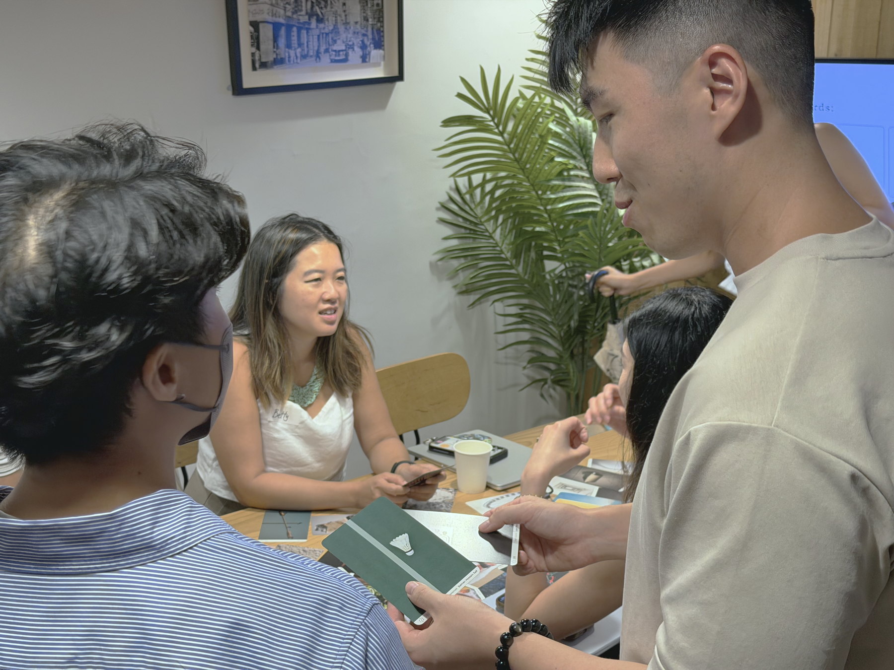 A close view from within a group conversation, one participant holding a card while another talks across the table.