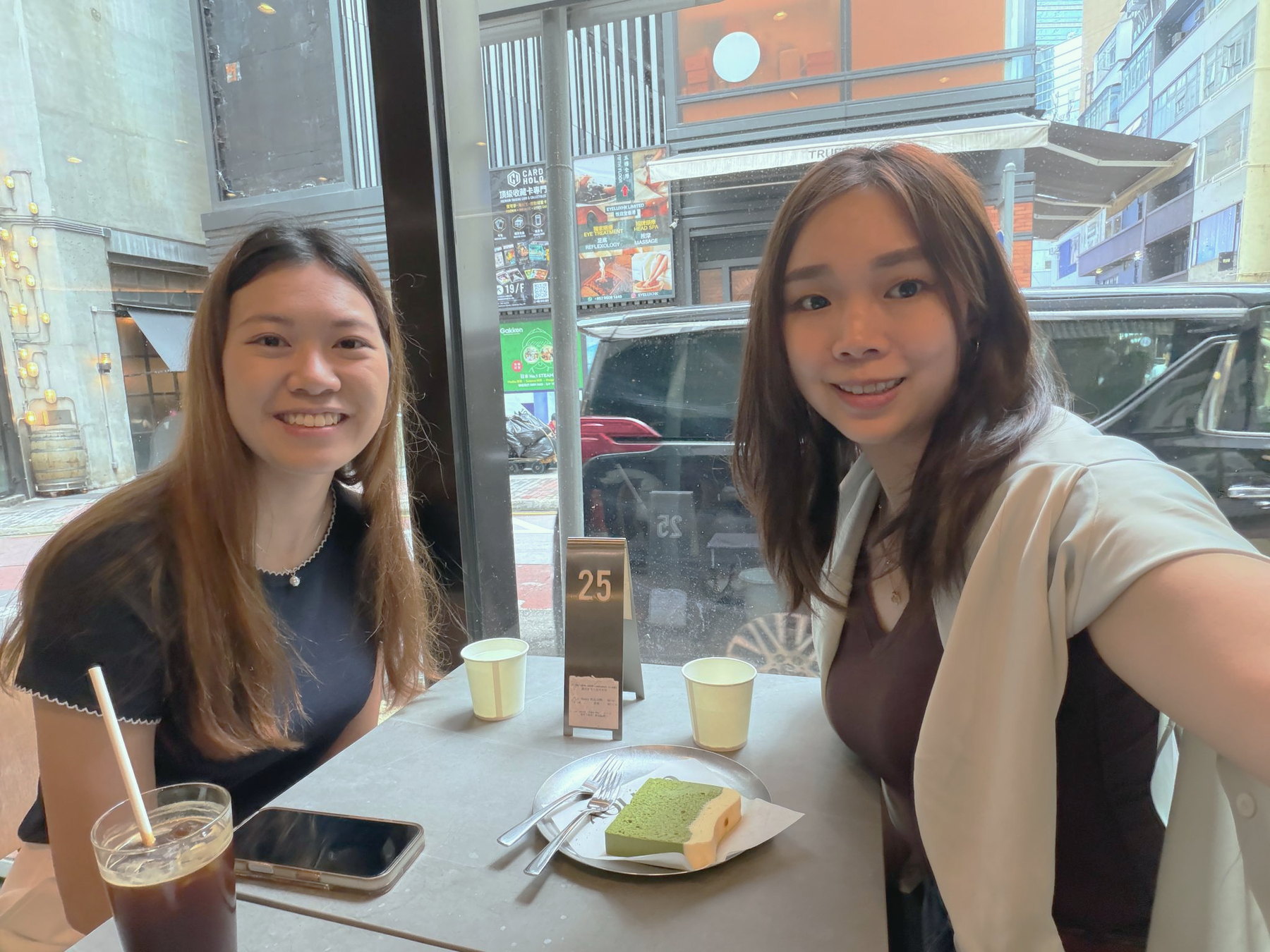 Zoe and Sharon sitting together at a café table by a window onto a Hong Kong street, catching up some months after the workshop.